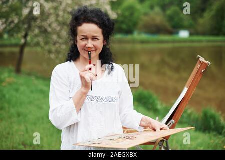 Having fun during the process. Portrait of mature painter with black curly hair in the park outdoors Stock Photo