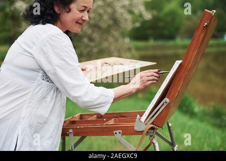 Positive woman. Portrait of mature painter with black curly hair in the park outdoors Stock Photo
