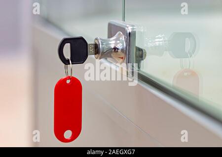 Lock with key with red tag on gray office glass furniture. Side view. Stock Photo