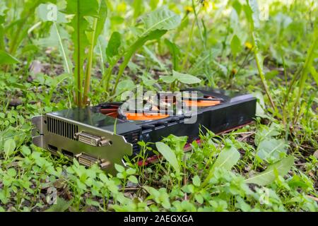 An old computer graphics card thrown into the street, lies in the grass and pollutes the nature Stock Photo