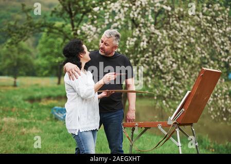 Having conversation. Mature couple have leisure days and working on the paint together in the park Stock Photo