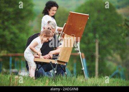 Changing colors. Grandmother and grandfather have fun outdoors with granddaughter. Painting conception Stock Photo