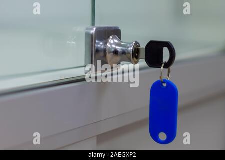 Lock with key with blue tag on gray office glass furniture. Side view. Stock Photo
