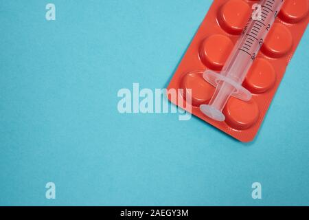 Empty syringe on an orange pills package on the turquoise surface. Medical background. Closeup with copy space. Coronavirus treatment. Stock Photo