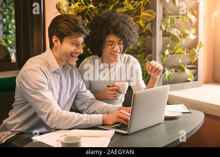 Happy millennial men looking at laptop in cafe Stock Photo