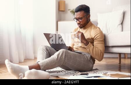 Man Using Laptop Having Coffee Sitting On Floor Indoor Stock Photo