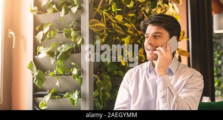 Cheerful guy talking via cellphone in cafe, panorama Stock Photo