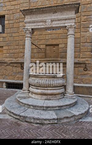 Well in front of a church wall at small square in Pienza , Siena province, Tuscany, Italy Stock Photo