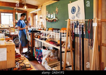 Japanese man wearing blue apron and glasses standing in a leather shop. Stock Photo