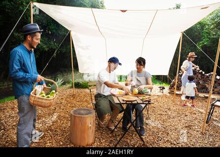 Group of Japanese men and women and boy gathered around a table under a canopy, preparing vegetables. Stock Photo