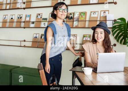 Two female Japanese professionals at a table in a co-working space, using laptop computer. Stock Photo