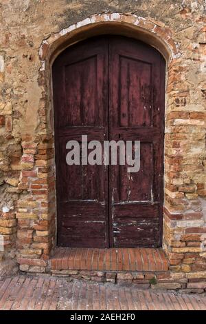 Architectural details of a weathered doors on an old brick house in a narrow winding streets at San Gimignano, Tuscany, Italy Stock Photo
