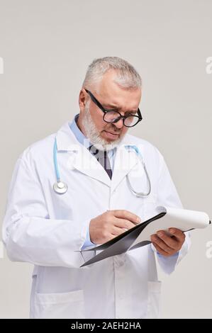 Mature doctor standing in white coat and writing a prescription isolated on white background Stock Photo