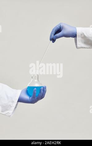 Close-up of scientist in protective gloves holding flask with blue liquid and analyzing samples isolated on white background Stock Photo