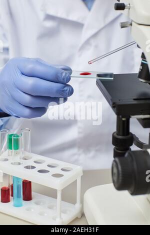 Close-up of doctor in gloves using pipette and working with blood samples using microscope Stock Photo