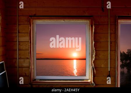The view from the window of a wooden country house on a colorful sunset over the lake. Summer house on the shore of the reservoir. Calmness and relaxa Stock Photo