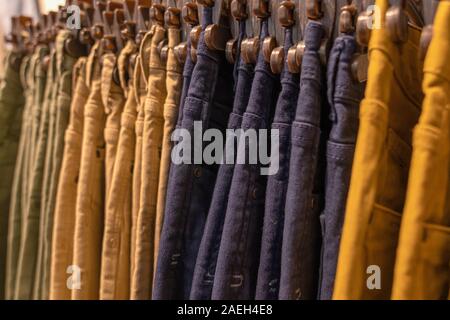jeans and pants of light warm colors, yellow, orange sand and mustard color hang in a row on a hanger in the store of fashionable youth brand modern c Stock Photo