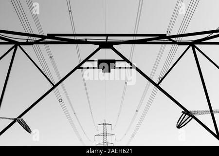 Black and white photo of electricity pylons and electricity cables silhouetted against the cloudless sky with leading lines Stock Photo