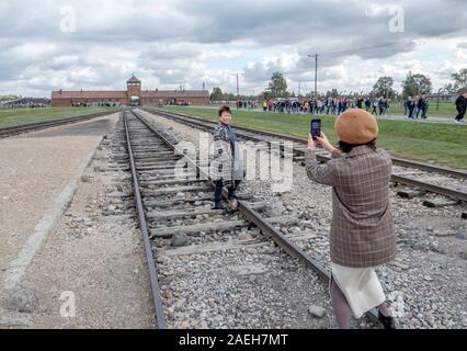 Auschwitz II-Birkenau. Tourists happilly pose for holiday photos on the railway. leading into Auschwitz II-Birkenau Death Camp. Building began in Octo Stock Photo