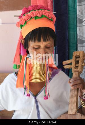 An eldery woman from Kayan tribe wearing traditional outfit and brass neck rings playing Kayan guitar with four strings in Pan Pet, Loikaw, Myanmar.
