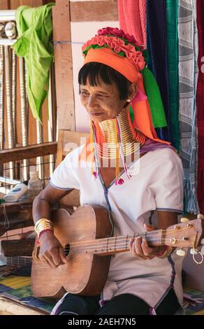 An eldery woman from Kayan tribe wearing traditional outfit and brass neck rings playing Kayan guitar with four strings in Pan Pet, Loikaw, Myanmar. Stock Photo