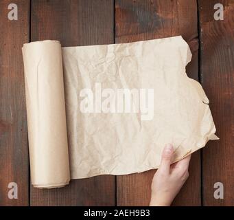 hand holds unfolded roll with brown parchment paper on wooden background, top view Stock Photo