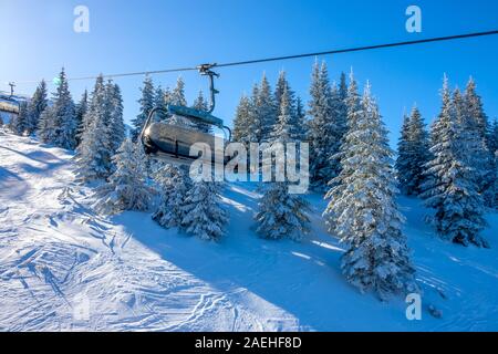 Winter sunny day on the mountainside. Snowy spruces and empty chair lift cabins Stock Photo