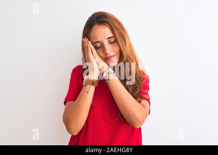 Young redhead woman wearing red casual t-shirt stading over white isolated background sleeping tired dreaming and posing with hands together while smi Stock Photo