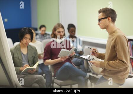 College student holding his report and presenting it to the audience while they making notes in notebooks Stock Photo