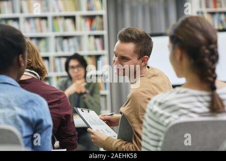 Young man with report talking to his colleagues during business presentation in the library Stock Photo
