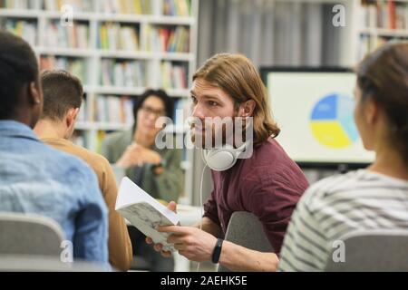 Young man holding book and discussing something with his colleagues during business seminar Stock Photo