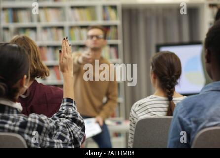 Rear view of young woman raised her hand she is going to ask the question to the speaker during presentation Stock Photo