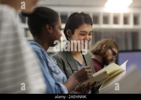 Two multiethnic students sitting together looking at their notebooks and discussing work together during lesson Stock Photo
