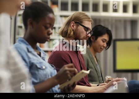 Multiethnic group of serious students concentrating on their writing while they sitting at lecture Stock Photo
