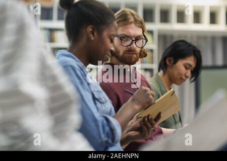 Young man in eyeglasses consulting with his colleague and she showing him her writings at lecture Stock Photo