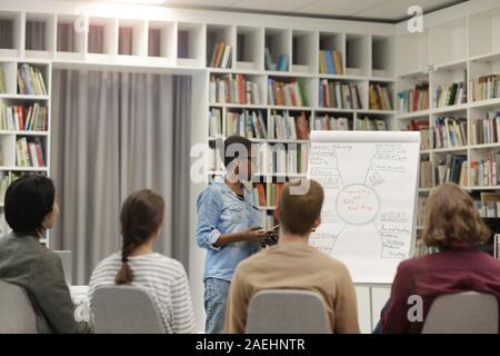 African young woman pointing at whiteboard and holding the presentation for young people in the library Stock Photo