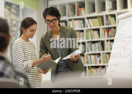Asian young teacher explaining something to student while she showing him the notebook during a lecture Stock Photo
