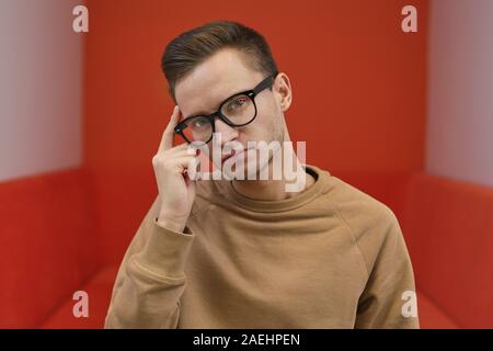 Portrait of young man in eyeglasses looking at camera and thinking about something Stock Photo