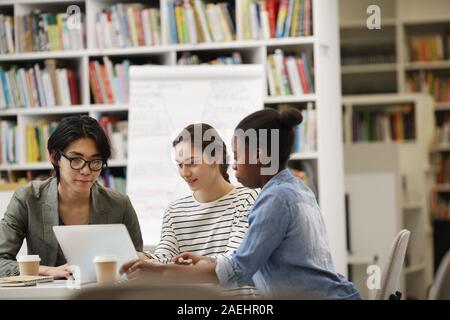Students sitting at the table and using laptop computer they doing homework together in the library Stock Photo