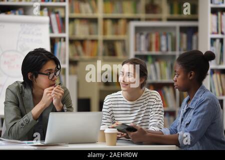 Multiethnic group of students sitting at the table with laptop and discussing homework together in team in the library Stock Photo