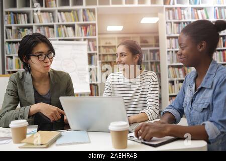 Group of young people sitting at the table with laptop and discussing new project in team in the library Stock Photo