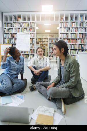 Group of young people sitting on the floor with papers and laptop and discussing their new project together they working in the library Stock Photo