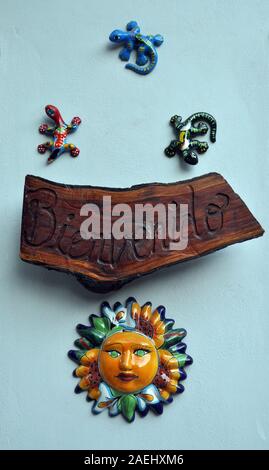 A wooden sign that reads 'Bienvenido'. It is surrounded by three ceramic salamander sand a colorful ceramic sun Stock Photo