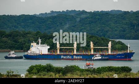 Bulk carrier ship Pacific Basin in the Gatun Lake being maneuvering by tugboats, waiting to enter the Gatun Locks Stock Photo