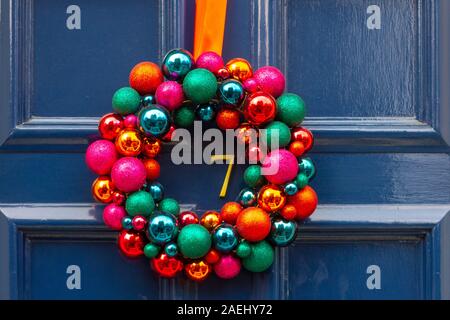 Colorful Christmas wreath made out of bright balls hanging on blue wooden front door with the house number 7 Stock Photo
