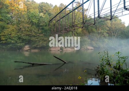 Rusted out abandoned train trestle over the river on a foggy misty morning with the sun rising showing the autumn colors Stock Photo