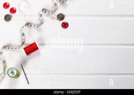 Flat lay of sewing equipment with cotton reels, buttons and measuring tape on a white background with space for text or design red and gold colours Stock Photo