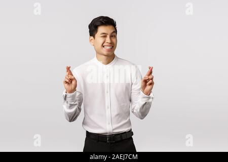 Cute hopeful optimistic asian male entrepreneur in white shirt, pants, wink camera cheeky, smiling assured everything be alright, cross fingers good Stock Photo