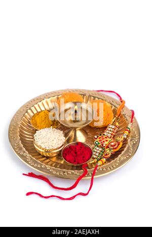 Indian Festival: Rakhi with rice grains, kumkum, sweets and diya on plate with an elegant Rakhi. A traditional Indian wrist band which is a symbol of Stock Photo