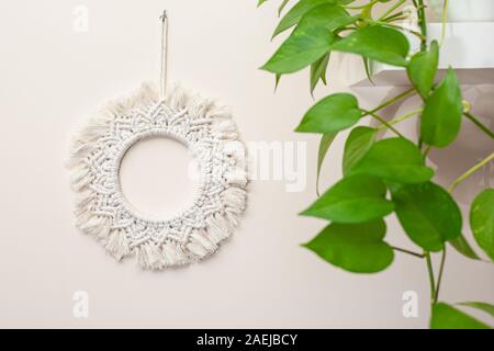 Handmade cotton macrame mandala wall decoration hanging on a wall with green leaves Stock Photo